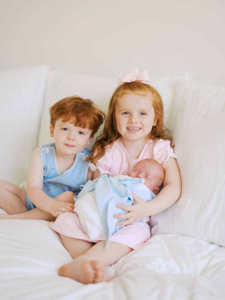 older sister and brother holding their little brother