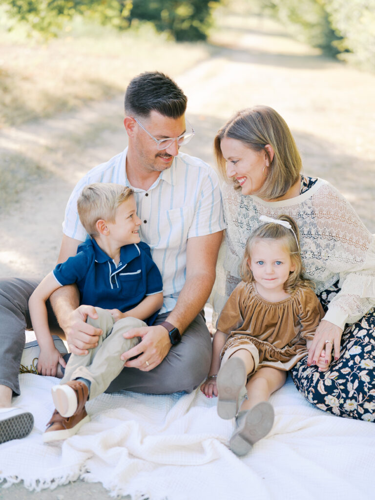 family of 4 sitting in blanket and smiling at each other